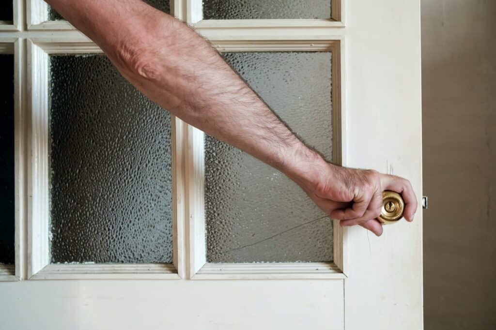Male hand closes a white painted wooden door with frosted glass in a country house